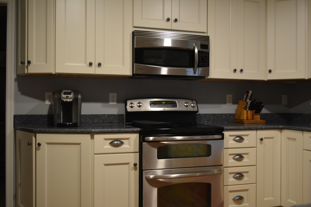 Example of a mid-sized transitional u-shaped dark wood floor and brown floor eat-in kitchen design with a farmhouse sink, shaker cabinets, beige cabinets, granite countertops, gray backsplash, mosaic tile backsplash, stainless steel appliances, a peninsula and black countertops
