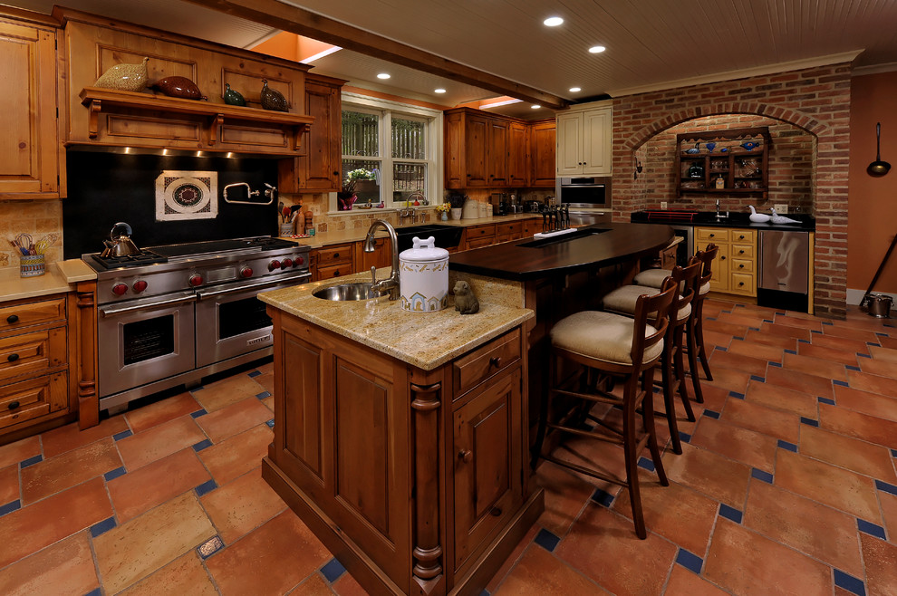 Design ideas for a large country u-shaped separate kitchen in DC Metro with an undermount sink, raised-panel cabinets, medium wood cabinets, granite benchtops, beige splashback, travertine splashback, stainless steel appliances, terra-cotta floors, with island, red floor and beige benchtop.