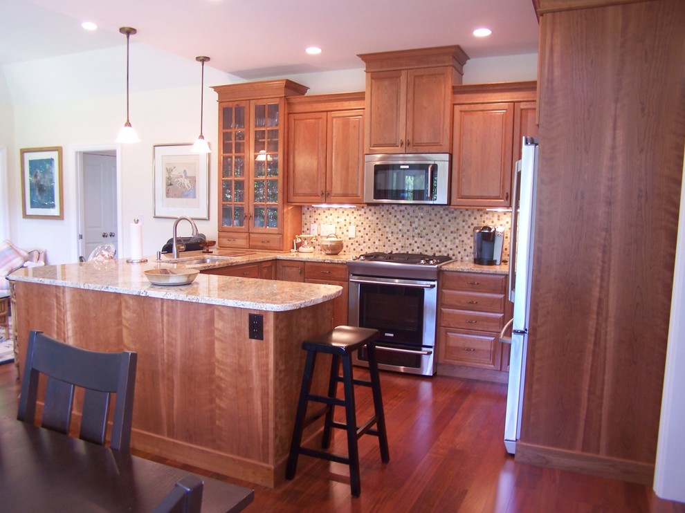 This is an example of a mid-sized traditional u-shaped open plan kitchen in Boston with an undermount sink, raised-panel cabinets, medium wood cabinets, granite benchtops, beige splashback, ceramic splashback, stainless steel appliances, dark hardwood floors and a peninsula.