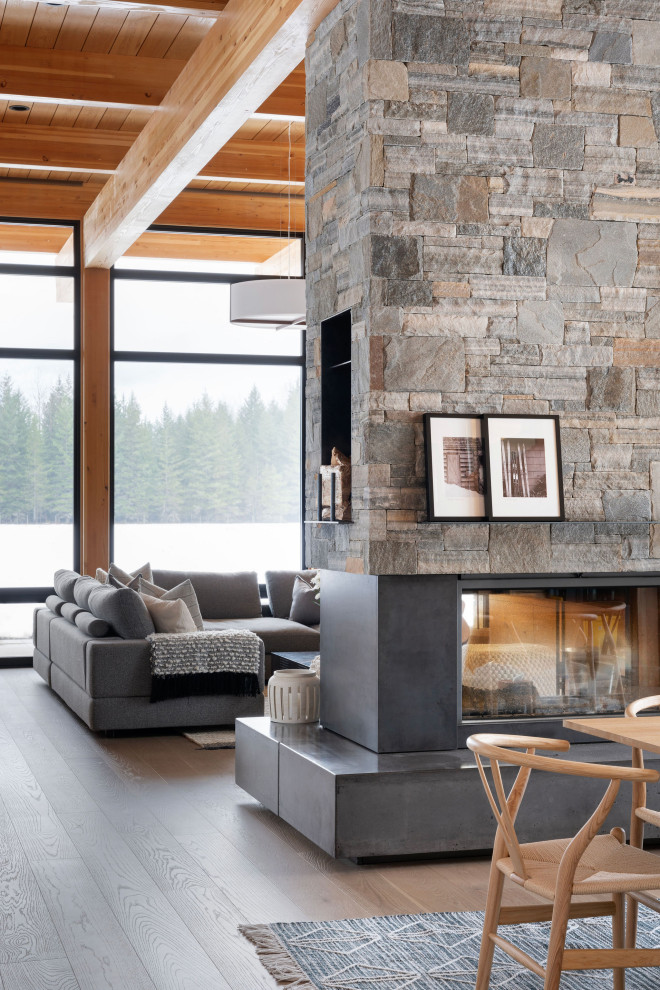 Example of a mid-sized mountain style open concept light wood floor, brown floor, wood ceiling and wood wall living room library design in Other with white walls, a two-sided fireplace, a stone fireplace and a wall-mounted tv
