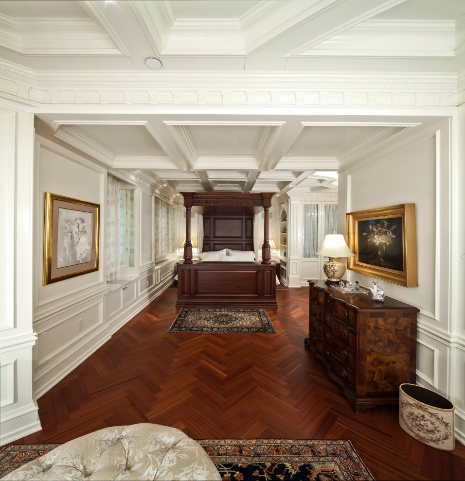 На фото: огромная хозяйская спальня в викторианском стиле с белыми стенами, паркетным полом среднего тона, коричневым полом, кессонным потолком и панелями на части стены без камина