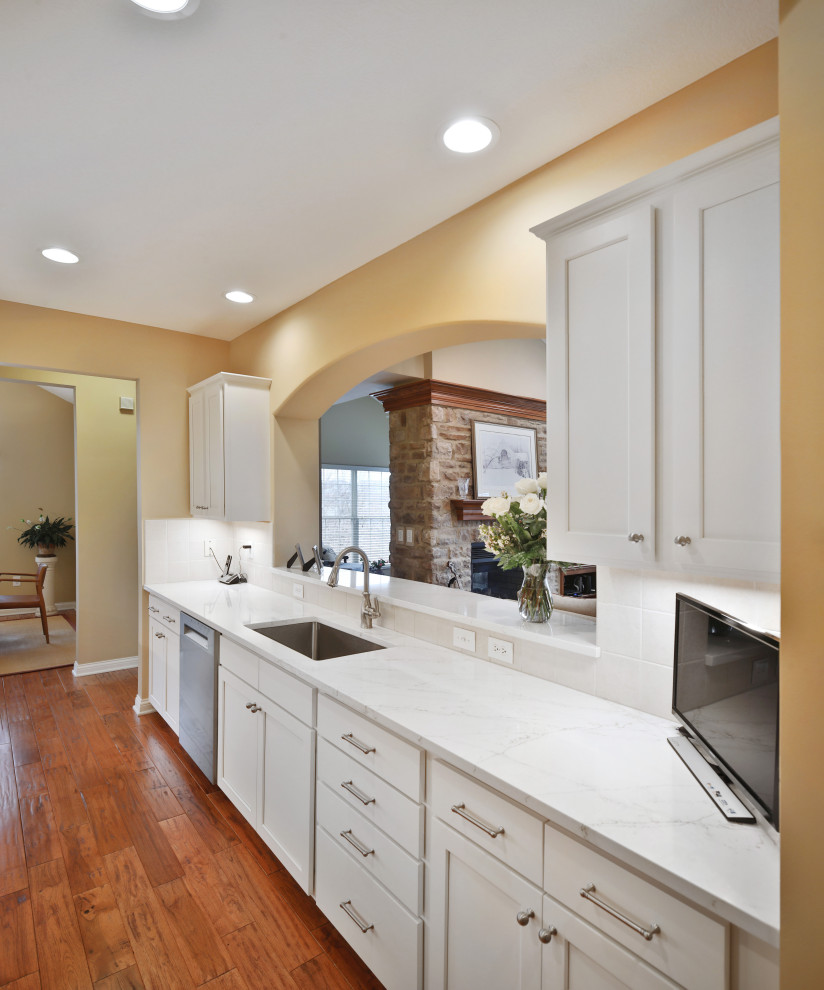 Example of a mid-sized transitional galley medium tone wood floor and brown floor enclosed kitchen design in Columbus with a single-bowl sink, shaker cabinets, white cabinets, quartz countertops, white backsplash, ceramic backsplash, stainless steel appliances, no island and white countertops