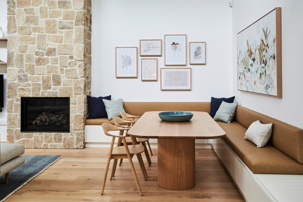 Immagine di una sala da pranzo contemporanea con pareti bianche, pavimento in compensato, camino classico, cornice del camino in pietra e pavimento marrone