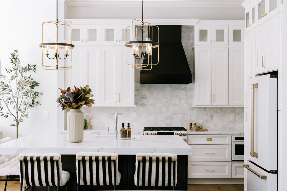 Klassisk inredning av ett stort vit vitt kök, med en nedsänkt diskho, luckor med profilerade fronter, vita skåp, bänkskiva i kvarts, grått stänkskydd, stänkskydd i marmor, vita vitvaror, mellanmörkt trägolv, en köksö och brunt golv