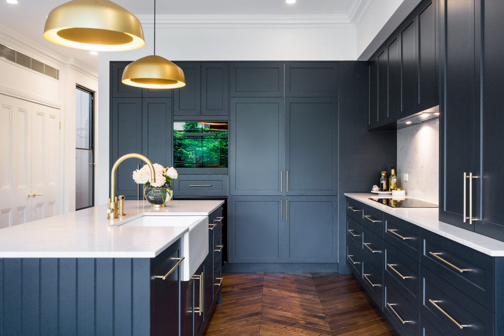 Transitional u-shaped kitchen in Melbourne with a farmhouse sink, shaker cabinets, black cabinets, quartz benchtops, multi-coloured splashback, medium hardwood floors, with island, brown floor and white benchtop.