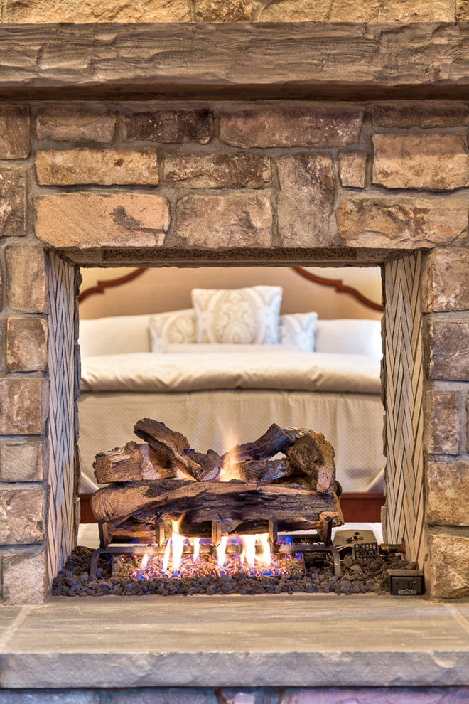 Large mountain style guest bedroom photo with a two-sided fireplace and a stone fireplace