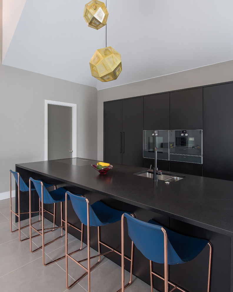 Inspiration for a mid-sized contemporary single-wall eat-in kitchen in London with a single-bowl sink, flat-panel cabinets, black cabinets, granite benchtops, black appliances, porcelain floors and with island.