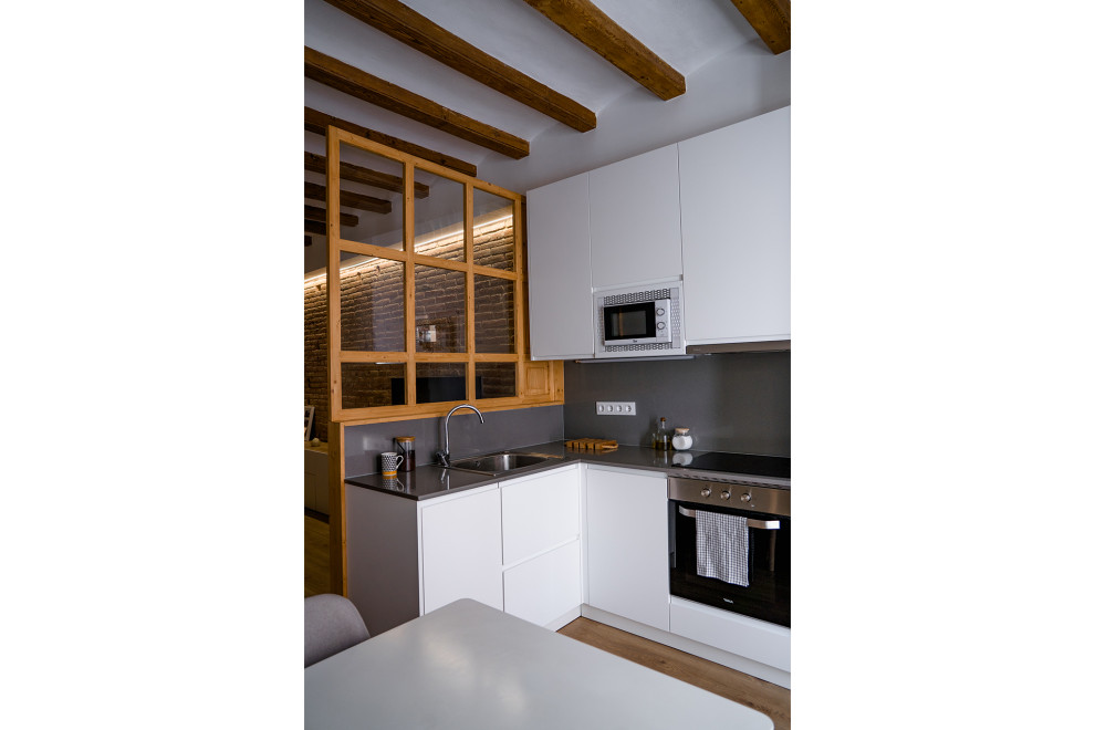 This is an example of a mid-sized country l-shaped open plan kitchen in Barcelona with flat-panel cabinets, white cabinets, quartz benchtops, grey splashback, engineered quartz splashback, stainless steel appliances, medium hardwood floors, a peninsula, brown floor, grey benchtop and exposed beam.