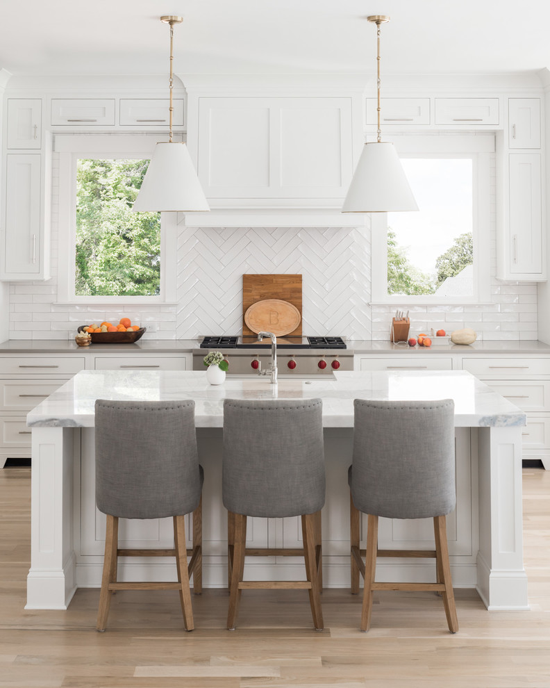 Inspiration for a transitional galley kitchen in Charlotte with a farmhouse sink, shaker cabinets, white cabinets, white splashback, subway tile splashback, stainless steel appliances, light hardwood floors, with island, beige floor and grey benchtop.