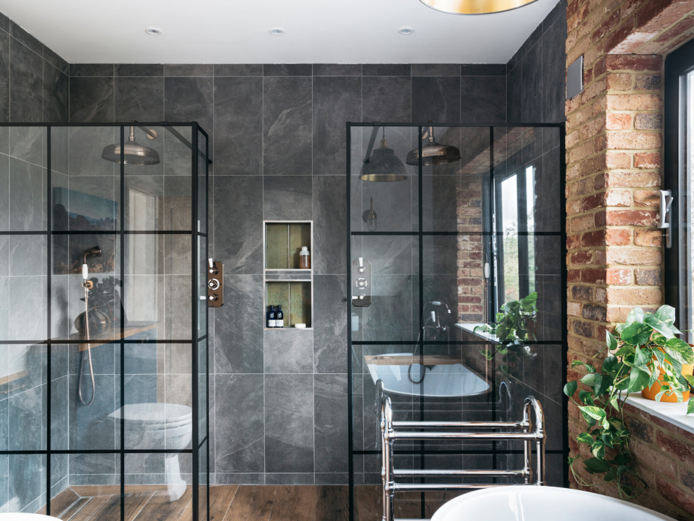 Design ideas for an expansive contemporary kids bathroom in London with flat-panel cabinets, distressed cabinets, a freestanding tub, an open shower, a one-piece toilet, gray tile, ceramic tile, ceramic floors, a wall-mount sink, wood benchtops, an open shower, brown benchtops, a double vanity, a floating vanity and brick walls.