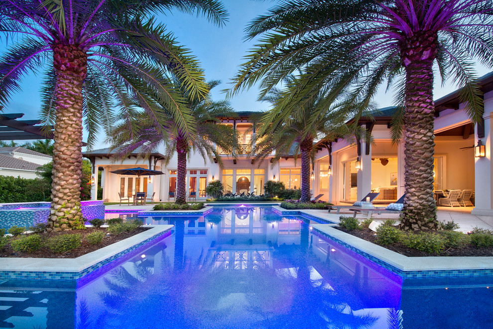 Inspiration for a large tropical backyard custom-shaped infinity pool in Miami with a hot tub and natural stone pavers.