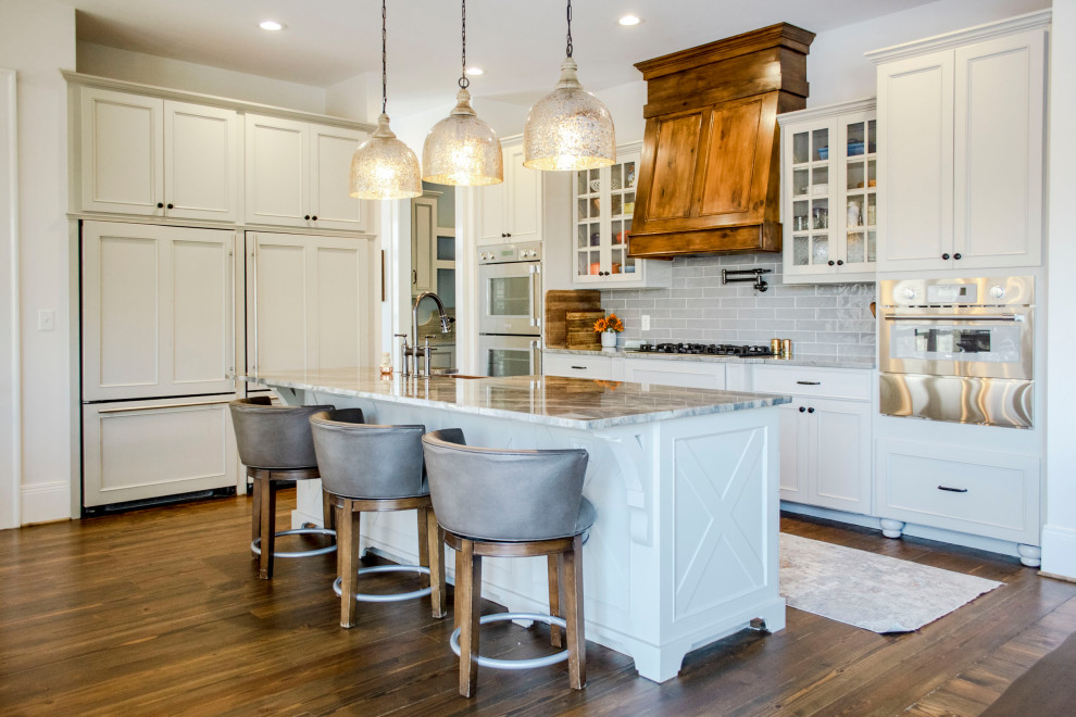 Elegant l-shaped dark wood floor and brown floor kitchen photo in Huntington with a farmhouse sink, recessed-panel cabinets, white cabinets, gray backsplash, subway tile backsplash, paneled appliances, an island and gray countertops