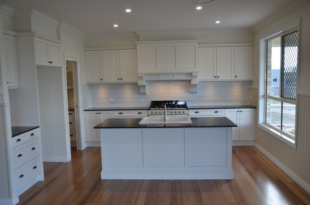 Photo of a mid-sized traditional galley eat-in kitchen in Brisbane with a farmhouse sink, shaker cabinets, distressed cabinets, granite benchtops, white splashback, porcelain splashback, coloured appliances, light hardwood floors and with island.