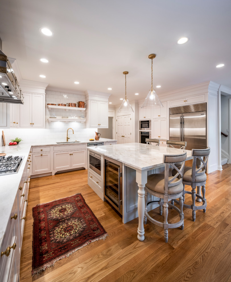 Open concept kitchen - large transitional l-shaped medium tone wood floor and brown floor open concept kitchen idea in Cincinnati with an undermount sink, white cabinets, marble countertops, white backsplash, subway tile backsplash, stainless steel appliances, an island, white countertops and shaker cabinets