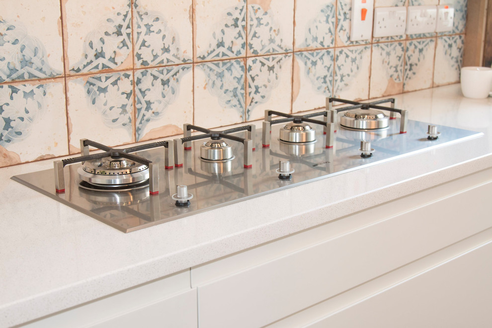 Small eclectic l-shaped home with a built-in sink, flat-panel cabinets, beige cabinets, quartz worktops, beige splashback, cement tile splashback, stainless steel appliances, laminate floors, an island and brown floors.