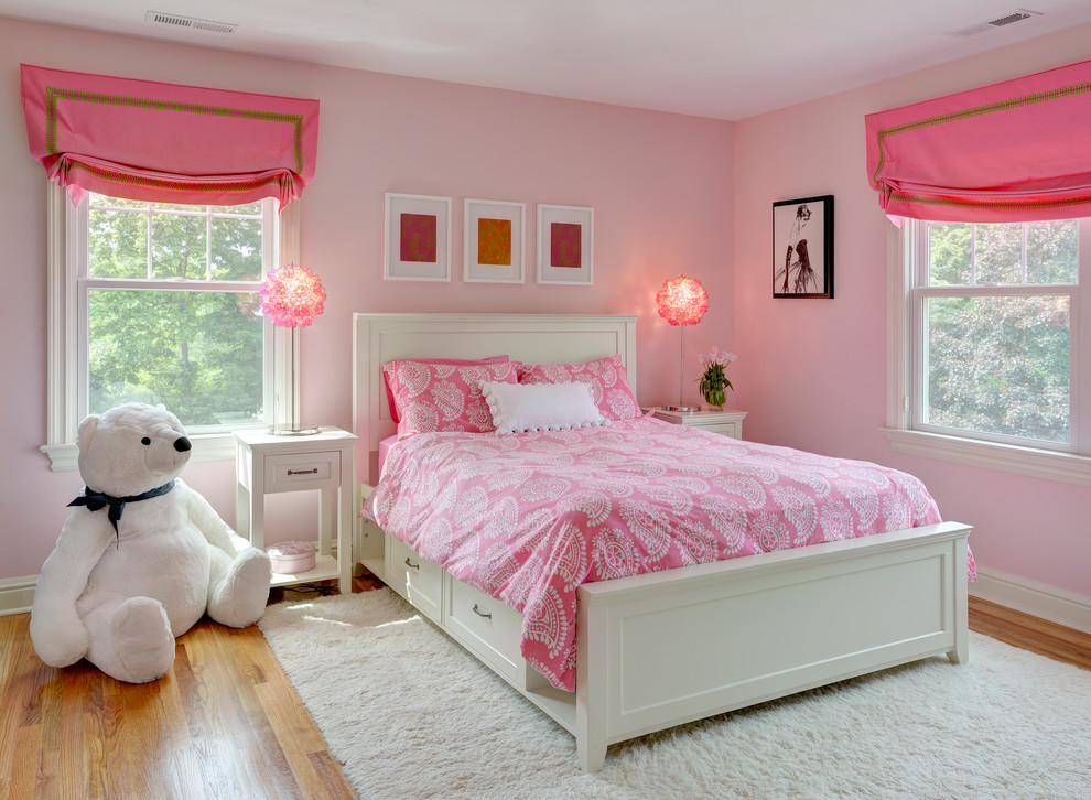 This is an example of a mid-sized transitional kids' bedroom for kids 4-10 years old and girls in New York with pink walls, medium hardwood floors and brown floor.