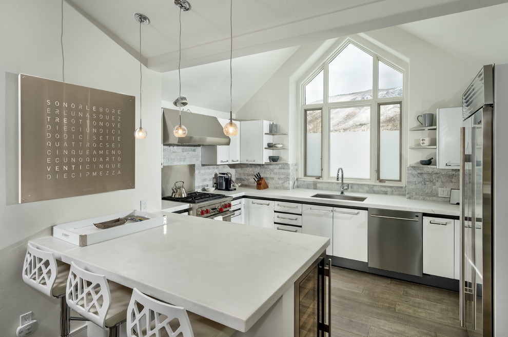 Example of a transitional kitchen design in Denver with an undermount sink, flat-panel cabinets, white cabinets, gray backsplash, stainless steel appliances and a peninsula