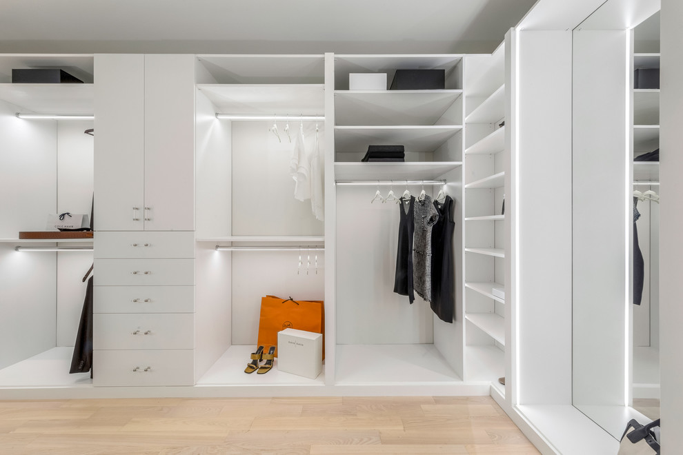 Photo of a large contemporary women's walk-in wardrobe in New York with flat-panel cabinets, white cabinets, light hardwood floors and beige floor.