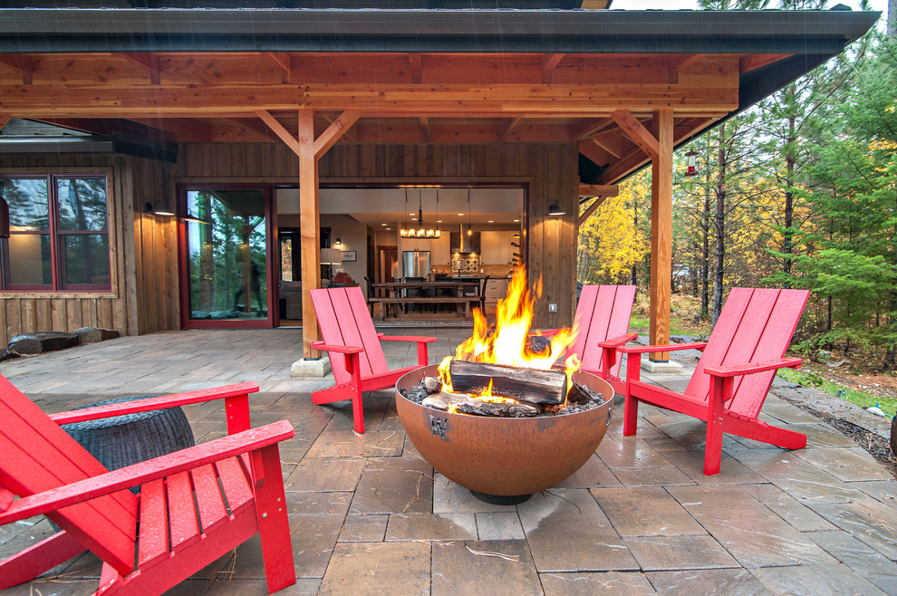 This is an example of a country backyard patio in Seattle with a fire feature, natural stone pavers and no cover.