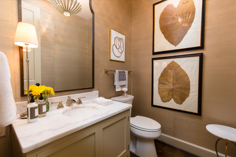 This is an example of a mid-sized traditional powder room in Birmingham with recessed-panel cabinets, beige cabinets, a two-piece toilet, beige walls, dark hardwood floors, an undermount sink, marble benchtops, brown floor and white benchtops.