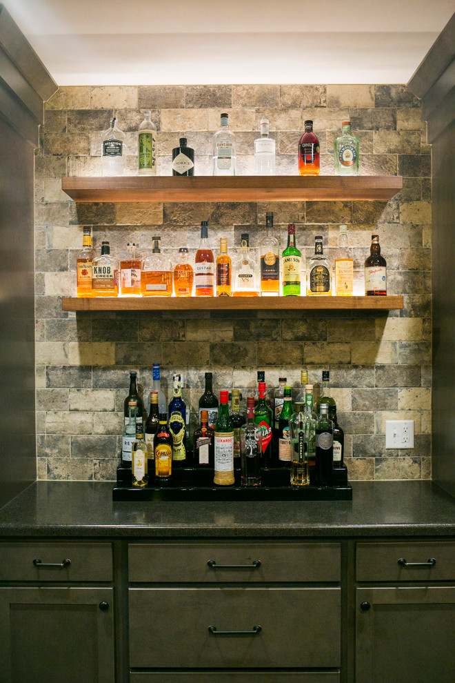 Photo of a large arts and crafts galley seated home bar in Other with a drop-in sink, recessed-panel cabinets, grey cabinets, solid surface benchtops, grey splashback, stone tile splashback, light hardwood floors, beige floor and grey benchtop.