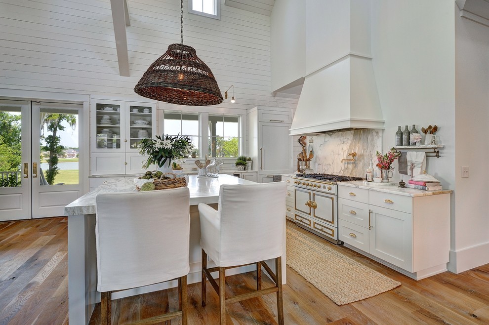 Inspiration for a large country l-shaped eat-in kitchen in Charleston with white cabinets, marble benchtops, white appliances, with island, grey splashback, stone slab splashback, medium hardwood floors and shaker cabinets.
