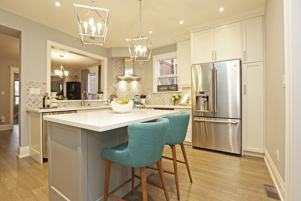 Mid-sized transitional u-shaped light wood floor and brown floor enclosed kitchen photo in Toronto with an undermount sink, shaker cabinets, white cabinets, solid surface countertops, gray backsplash, stainless steel appliances, an island and white countertops