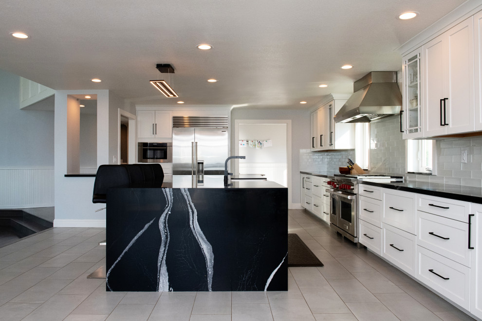 Design ideas for a large modern galley open plan kitchen in Sacramento with a single-bowl sink, shaker cabinets, white cabinets, quartz benchtops, white splashback, subway tile splashback, stainless steel appliances, porcelain floors, with island, grey floor and black benchtop.