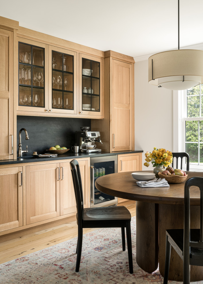 Inspiration for a large transitional u-shaped medium tone wood floor eat-in kitchen remodel in Burlington with an undermount sink, shaker cabinets, light wood cabinets, soapstone countertops, black backsplash, stone slab backsplash, an island and black countertops
