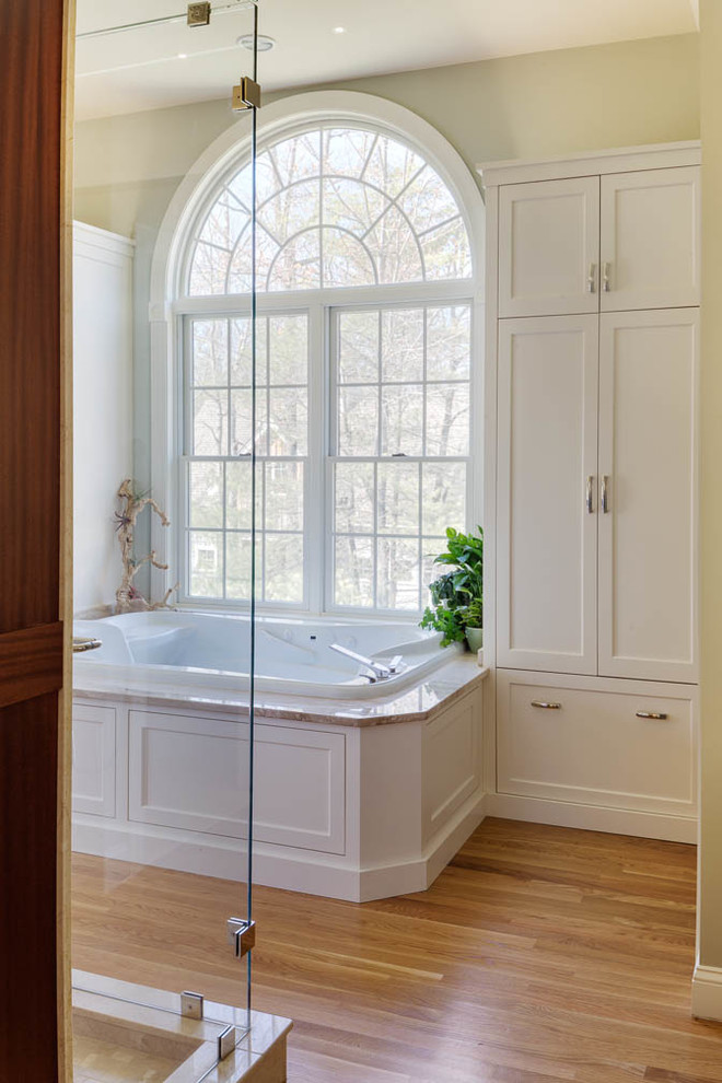 Photo of a large transitional bathroom in Boston with flat-panel cabinets, white cabinets, a hot tub, an alcove shower, beige tile, glass tile, medium hardwood floors, an undermount sink and marble benchtops.