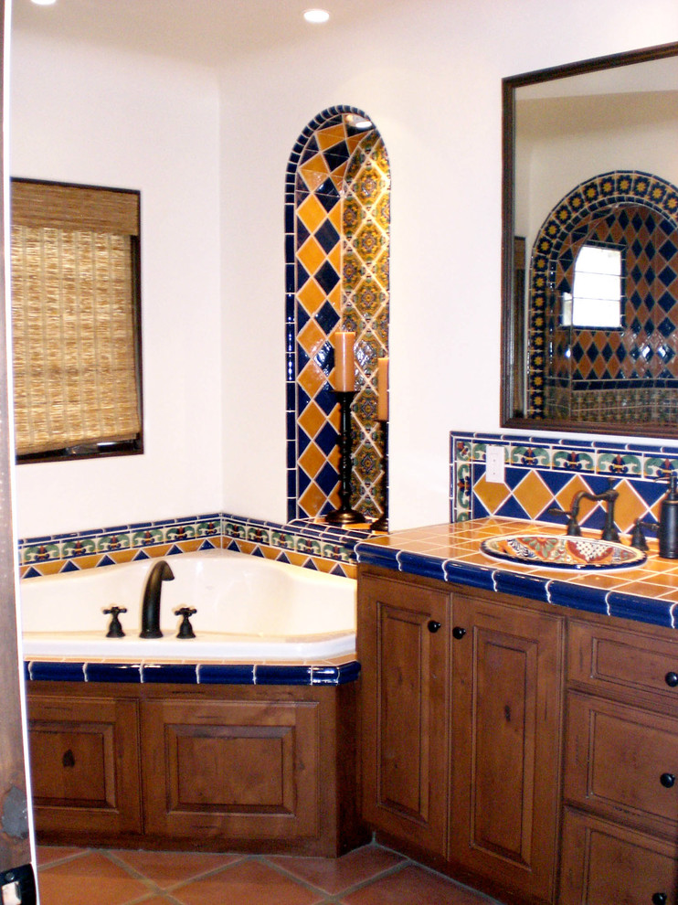 Design ideas for a mid-sized mediterranean master bathroom with raised-panel cabinets, medium wood cabinets, tile benchtops, ceramic tile, an open shower, a one-piece toilet, a drop-in sink, white walls, a corner tub, blue tile, yellow tile and terra-cotta floors.