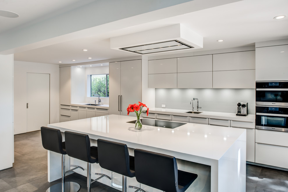 Design ideas for a mid-sized modern galley open plan kitchen in San Francisco with an undermount sink, flat-panel cabinets, white cabinets, quartz benchtops, white splashback, glass sheet splashback, stainless steel appliances, ceramic floors, with island and grey floor.
