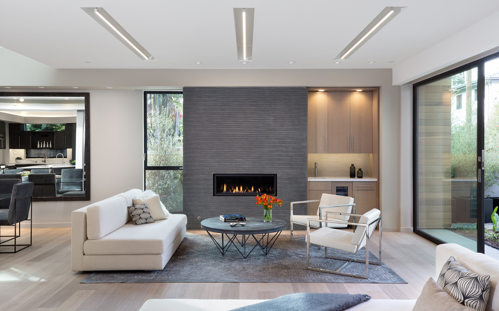 Inspiration for a contemporary open concept living room in Los Angeles with beige walls, light hardwood floors, a ribbon fireplace, a tile fireplace surround, no tv and beige floor.