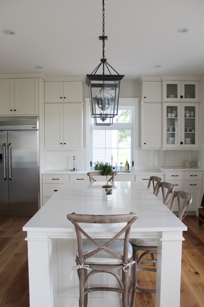 Inspiration for a large transitional l-shaped eat-in kitchen remodel in Toronto with an undermount sink, shaker cabinets, white cabinets, quartz countertops, white backsplash, stainless steel appliances and an island