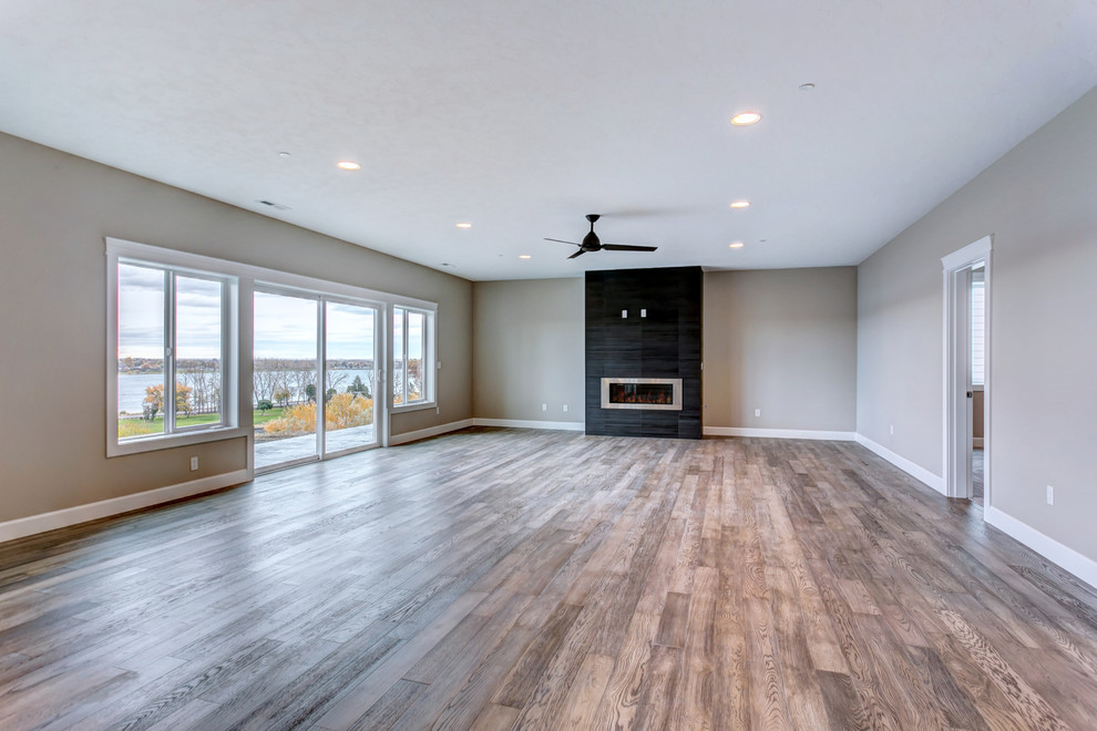This is an example of a large transitional walk-out basement in Seattle with grey walls, light hardwood floors, a ribbon fireplace, a tile fireplace surround and grey floor.