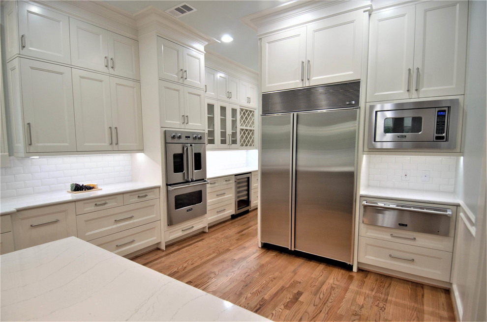 Photo of an expansive transitional kitchen in Houston with an undermount sink, shaker cabinets, white cabinets, quartz benchtops, white splashback, subway tile splashback, stainless steel appliances, medium hardwood floors, with island and brown floor.