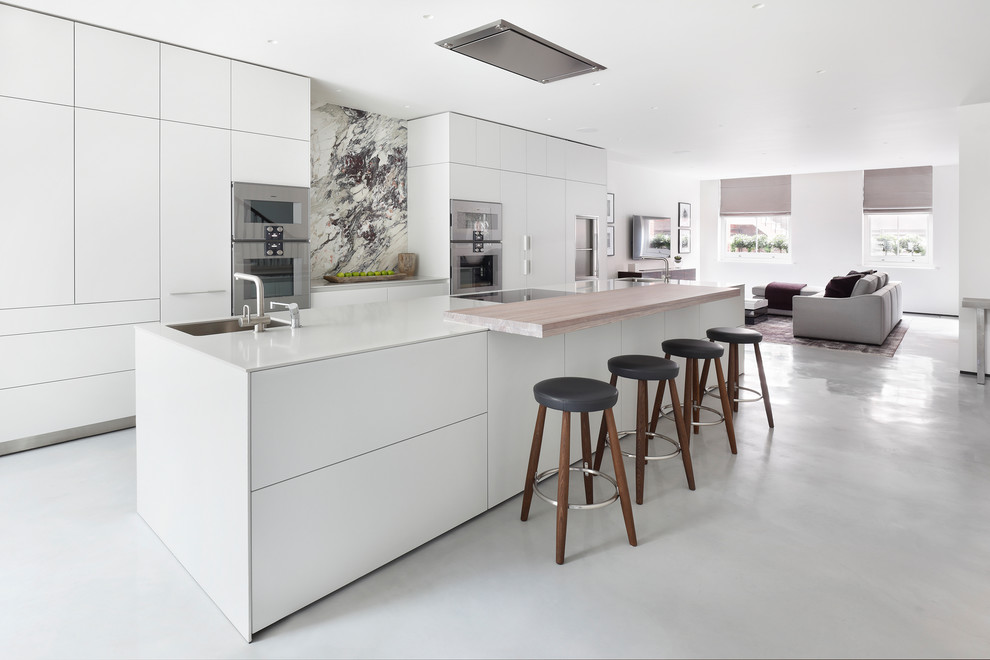 Photo of a mid-sized contemporary galley open plan kitchen in London with an undermount sink, flat-panel cabinets, white cabinets, grey splashback, stainless steel appliances, with island, grey floor, white benchtop, quartzite benchtops, marble splashback and concrete floors.