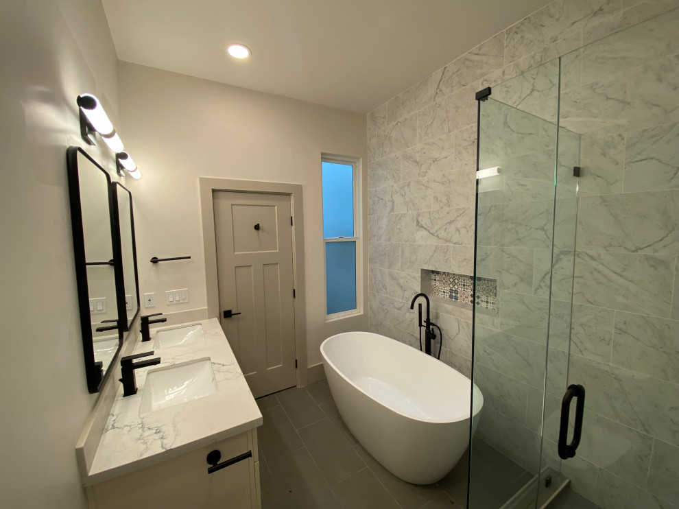 Bild på ett mellanstort 50 tals vit vitt badrum, med vita skåp, ett fristående badkar, en toalettstol med separat cisternkåpa, klinkergolv i porslin, ett nedsänkt handfat och grått golv