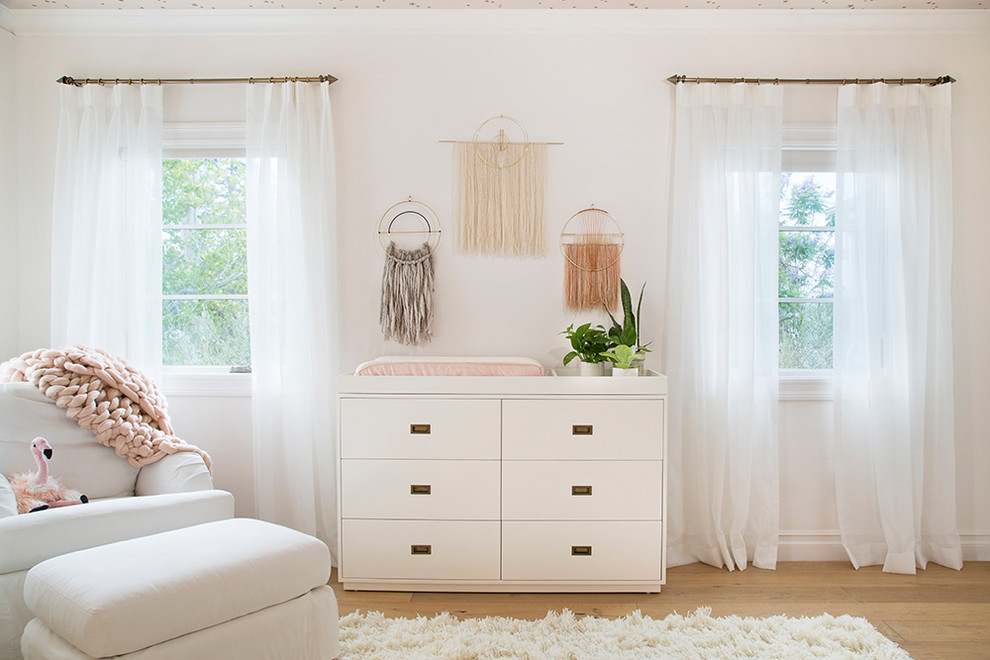 Design ideas for a mid-sized modern nursery for girls in Los Angeles with white walls and medium hardwood floors.