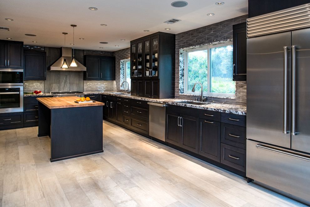 This is an example of a large contemporary l-shaped open plan kitchen in Sacramento with an undermount sink, flat-panel cabinets, granite benchtops, grey splashback, porcelain splashback, stainless steel appliances, porcelain floors, with island, beige floor, black cabinets and grey benchtop.