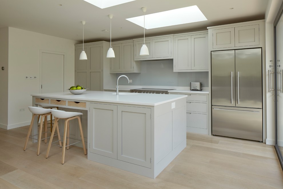 Design ideas for a medium sized contemporary single-wall open plan kitchen in Surrey with an integrated sink, shaker cabinets, grey cabinets, engineered stone countertops, white splashback, glass sheet splashback, stainless steel appliances, light hardwood flooring, an island and beige floors.
