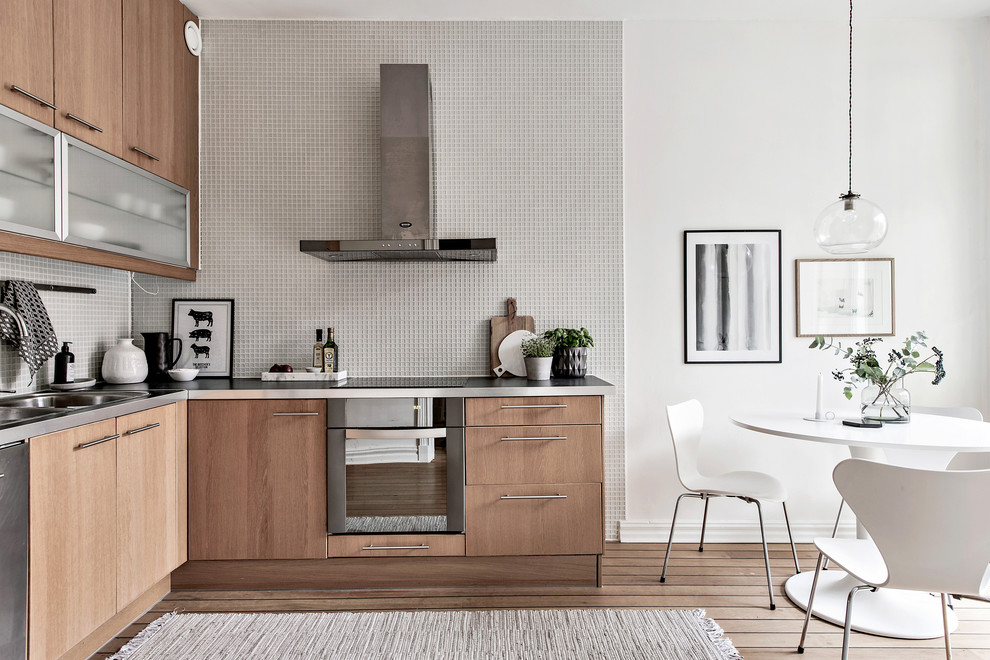 Design ideas for a scandinavian l-shaped eat-in kitchen in Gothenburg with a drop-in sink, flat-panel cabinets, light wood cabinets, mosaic tile splashback, stainless steel appliances, light hardwood floors and white splashback.