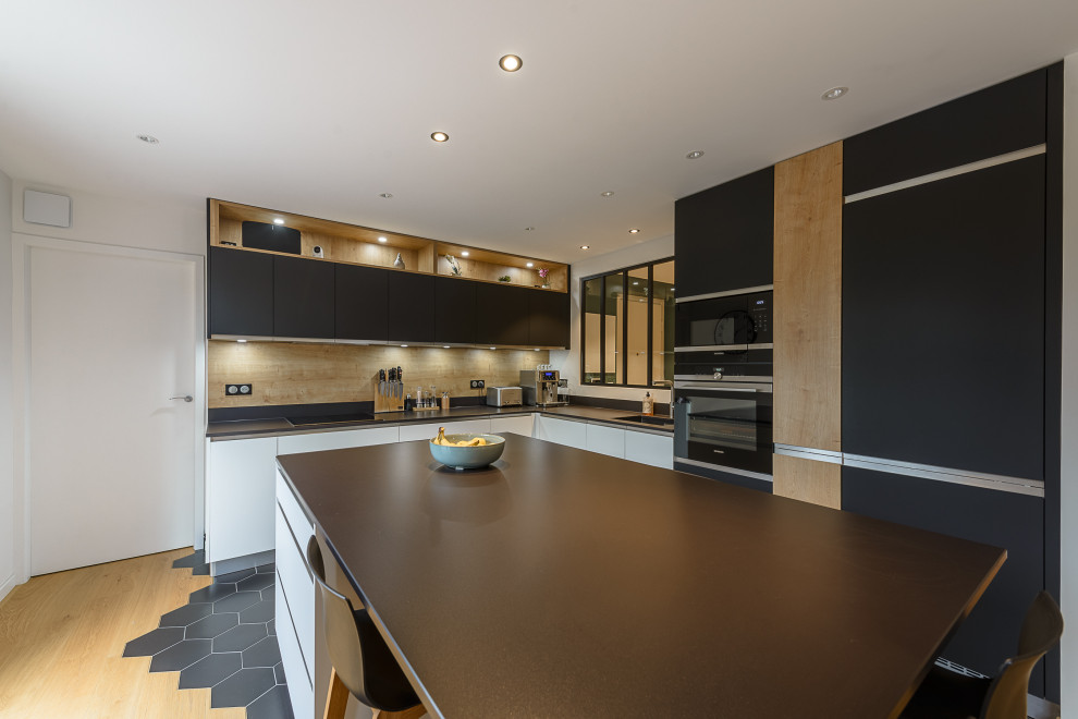 Inspiration for a large contemporary l-shaped eat-in kitchen in Lyon with timber splashback, stainless steel appliances, light hardwood floors, with island, black floor and black benchtop.