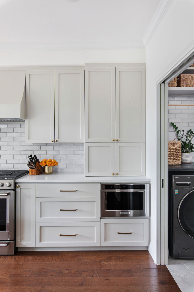 Mid-sized transitional medium tone wood floor and brown floor open concept kitchen photo in Austin with an undermount sink, shaker cabinets, gray cabinets, quartz countertops, white backsplash, brick backsplash, stainless steel appliances, a peninsula and white countertops