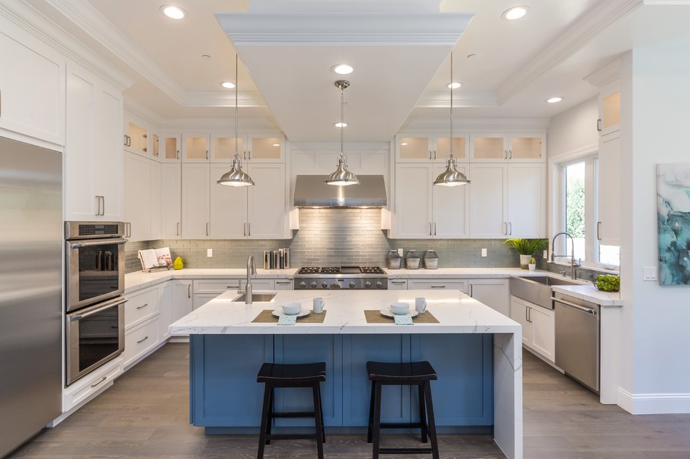 Inspiration for a contemporary u-shaped eat-in kitchen in San Francisco with a farmhouse sink, shaker cabinets, white cabinets, quartz benchtops, grey splashback, glass tile splashback, stainless steel appliances, with island, grey floor, white benchtop and medium hardwood floors.