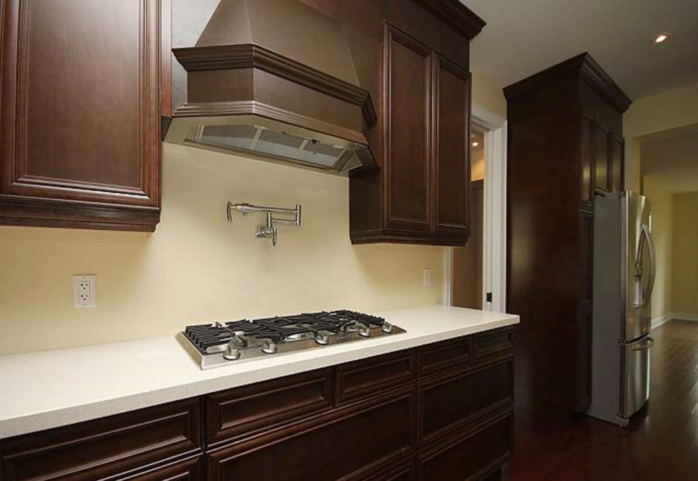 Mid-sized transitional l-shaped dark wood floor and brown floor kitchen photo in Toronto with an undermount sink, recessed-panel cabinets, dark wood cabinets, solid surface countertops, stainless steel appliances and an island