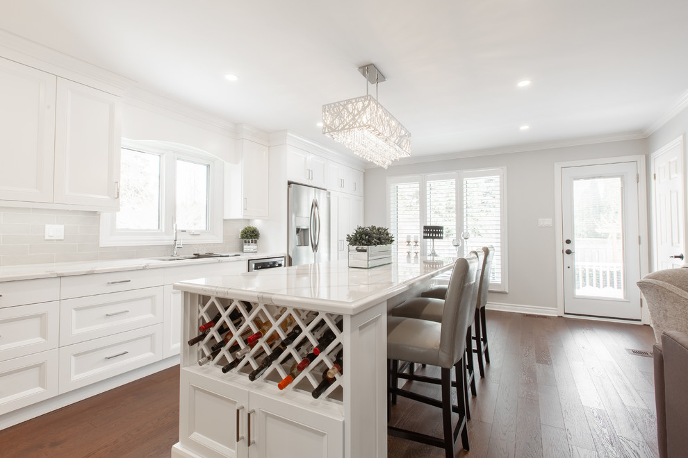 Inspiration for a large transitional l-shaped medium tone wood floor and brown floor enclosed kitchen remodel with an undermount sink, recessed-panel cabinets, white cabinets, quartz countertops, gray backsplash, ceramic backsplash, stainless steel appliances, an island and white countertops