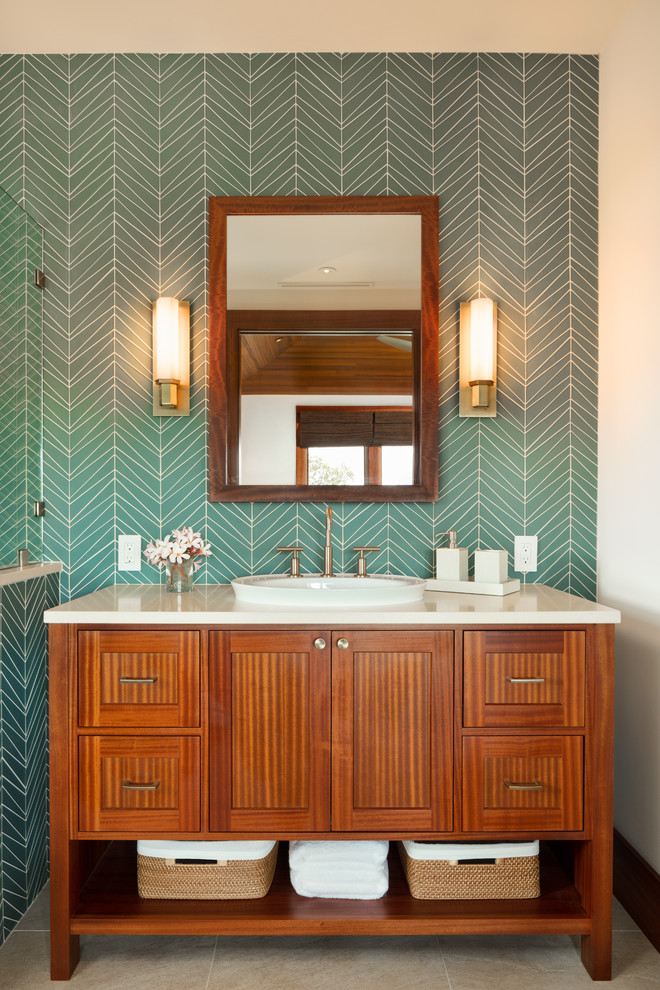 This is an example of a mid-sized tropical master bathroom in Hawaii with medium wood cabinets, a corner shower, a one-piece toilet, blue tile, glass tile, white walls, ceramic floors, a drop-in sink, engineered quartz benchtops, beige floor, an open shower and shaker cabinets.