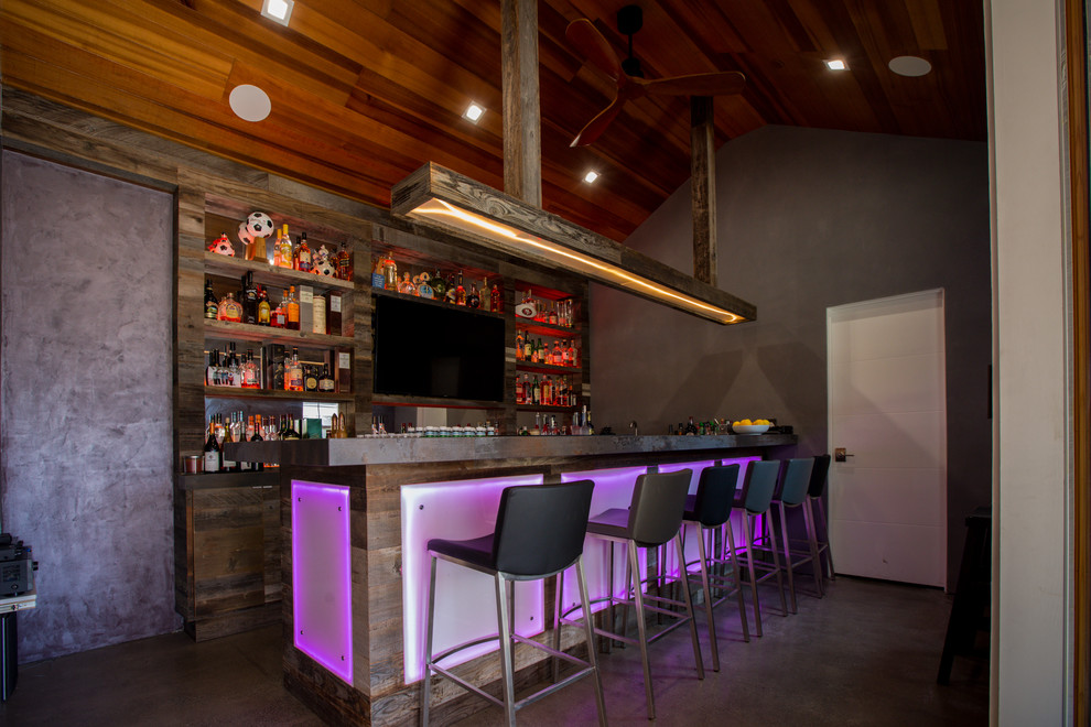 Photo of a mid-sized industrial u-shaped seated home bar in San Francisco with an undermount sink, open cabinets, distressed cabinets, concrete benchtops, timber splashback, concrete floors, grey floor and grey benchtop.