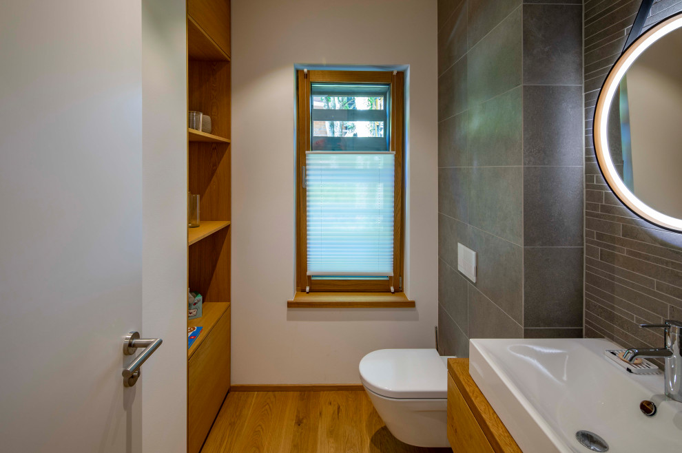 Immagine di un bagno di servizio minimal con ante in legno scuro, WC sospeso, piastrelle grigie, pavimento in legno massello medio e top marrone